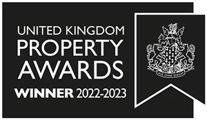 The image shows a black and white banner with the text "United Kingdom Property Awards" and "Winner 2022-2023." It also features a detailed crest or coat of arms on the right side, enclosed in a ribbon-like shape.