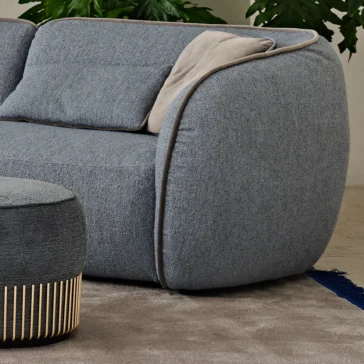 Contemporary Bouclè Modular Corner Sofa The Contemporary Bouclè Modular Corner Sofa in plush gray with rounded edges and light gray cushion sits on a beige carpet, accented by a hint of blue rug, while lush green plant leaves create a serene backdrop.