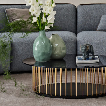 Contemporary Bouclè Modular Corner Sofa In a modern living room, the Contemporary Bouclè Modular Corner Sofa in grey is paired with a round black coffee table adorned with vertical gold bars, a ceramic elephant figurine, two vases filled with white flowers, and complemented by a green plant for a natural touch.
