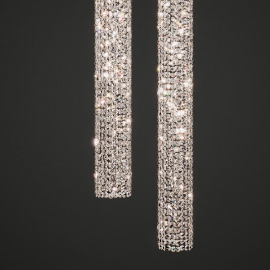 Two cylindrical Luxury Vertical Crystal LED Chandeliers suspended against a black backdrop, showcasing their numerous sparkling crystals that create a dazzling and elegant light display. The crystals catch and reflect light magnificently, enhancing their shimmer and brilliance.