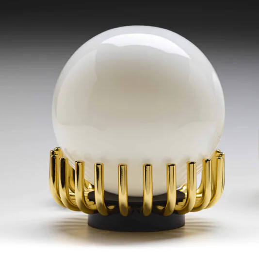 Small Contemporary Sphere Table Lamp The Small Contemporary Sphere Table Lamp showcases a large, spherical white glass bulb supported by a stylish gold-colored metal base with a comb-like design. The background features a gradient gray, transitioning from dark at the top to light at the bottom.