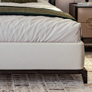 Art Deco Style Bed With Tall Headboard The Art Deco Style Bed With Tall Headboard features a neatly made arrangement with white bedding and a green and gold patterned blanket at the foot. It has a white upholstered base supported by dark wooden legs. On the right, a bedside table adorned with a book and showcasing a gold geometric design is partially visible.
