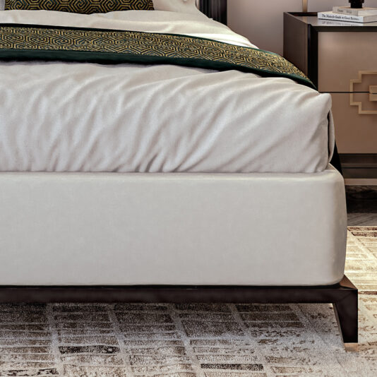 Art Deco Style Bed With Tall Headboard The Art Deco Style Bed With Tall Headboard features a neatly made arrangement with white bedding and a green and gold patterned blanket at the foot. It has a white upholstered base supported by dark wooden legs. On the right, a bedside table adorned with a book and showcasing a gold geometric design is partially visible.