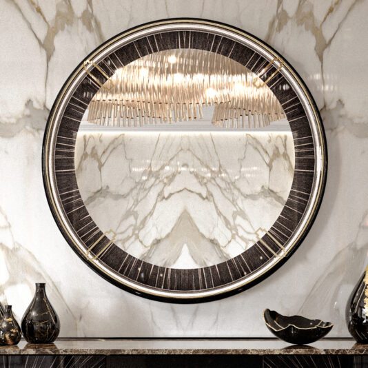 A Backlit Art Deco Style Veneer Round Mirror with a thick, dark frame hangs on a marble wall. The reflection in the mirror shows a modern chandelier with numerous small lights. Below the mirror is a dark tabletop adorned with decorative items, including vases and a shallow bowl.
