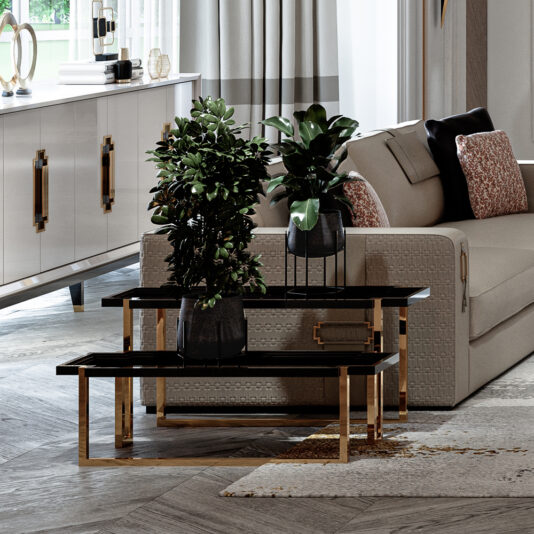 A modern living room featuring a beige sofa adorned with pillows, a set of black nested coffee tables with gold legs holding potted plants, and the High End Double Tiered End Table by the white sideboard with gold handles. Light gray curtains frame the large window, and wood-patterned tiles cover the floor.