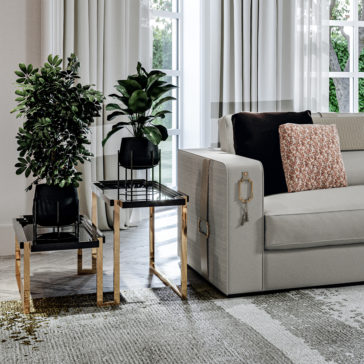 High End Double Tiered End Table A modern living room features a light gray sofa decorated with black and patterned throw pillows. Two potted plants are placed on High End Double Tiered End Tables, which boast gold accents and black tops. Floor-to-ceiling windows draped with sheer white curtains let natural light flood the room.
