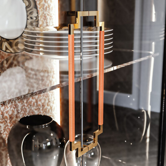 High End Glass Display Cabinet A High End Glass Display Cabinet with a golden frame and rectangular handles showcases dishes neatly stacked on a glass shelf. Below, a decorative plate and two black vases add elegance against the backdrop of a textured wall.