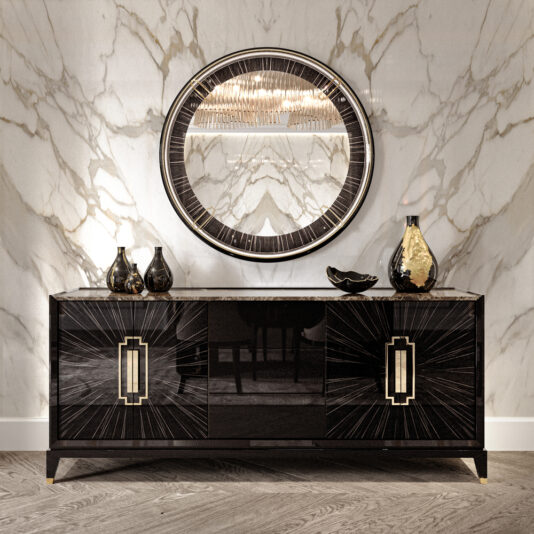 High End Veneer And Marble Sideboard A marble wall features a large, round mirror with a dark frame and gold accents, reflecting light. Below the mirror is the High End Veneer And Marble Sideboard adorned with geometric designs. The sleek black and gold table holds three vases and a small decorative dish, set on a wooden floor.