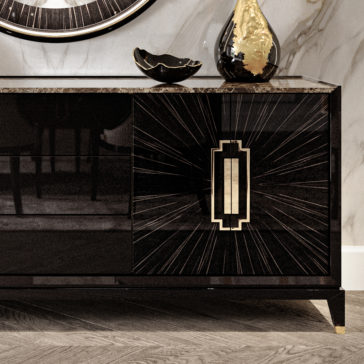 The High-End Veneer and Marble Sideboard, featuring a modern black and gold finish with a sunburst pattern on its doors, stands against a marble wall. A black bowl and decorative vase adorn its granite countertop. The sideboard is distinguished by its polished surface and sleek, geometric handles.