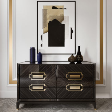 High End Veneer Chest Of Drawers A modern interior showcases a High End Veneer Chest Of Drawers adorned with gold accents. This piece is crowned with blue and black decorative vases and orbs. Hanging above it is an abstract black and gold art piece. The room's white walls are enhanced with intricate gold and white trim detailing.