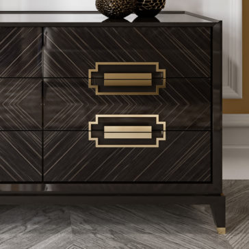 High End Veneer Chest Of Drawers The High End Veneer Chest of Drawers showcases a dark wooden design with a striking herringbone pattern and elegant gold geometric handles. This sophisticated dresser includes two spacious drawers and is complemented by decorative textured spheres on top. It stands gracefully on a light-colored hardwood floor, enhancing the ambiance of the modern room around it.