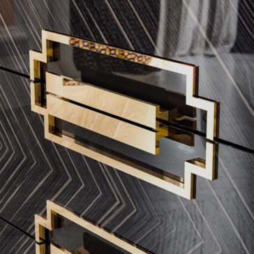 High End Veneer Chest Of Drawers A sleek, geometric gold handle is mounted on the glossy, dark chevron-patterned surface of the