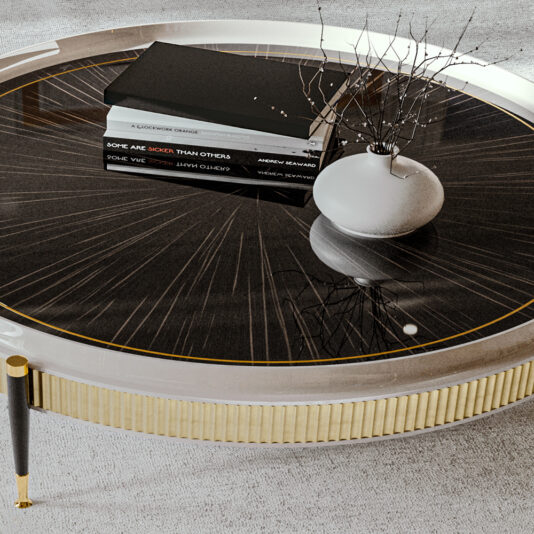 High End Veneered Low Round Coffee Table The High End Veneered Low Round Coffee Table boasts a sophisticated black, glossy surface adorned with a sunburst pattern. It is complemented by a small white vase containing bare twigs and a neatly stacked trio of books. Gold accents further enhance the table's elegance, which gracefully stands on a light-colored, textured rug.