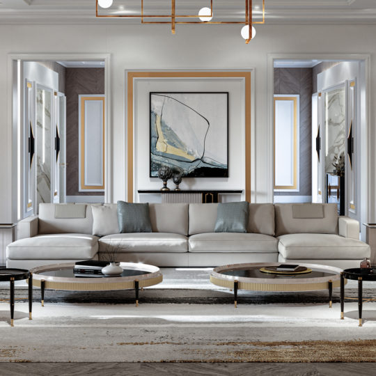 Modern living room with a high-end *Large Chaise Art Deco Style Sofa* adorned with blue and grey accent pillows, facing two round coffee tables. A large abstract painting is centered on the back wall, which features gold and white decorative trim. The room is brightly lit and elegant.