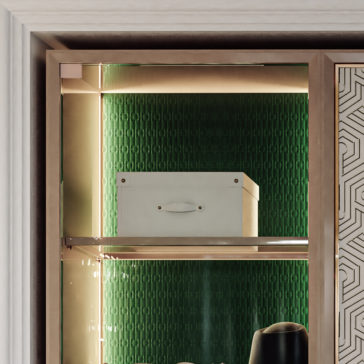 Large High End Integrated Wardrobe A close-up image highlights a section of the Large High-End Integrated Wardrobe, featuring a glass door. Inside, on the top shelf against a green textured background, rests a white rectangular box. The right side of the frame reveals part of a patterned door and a round black object.
