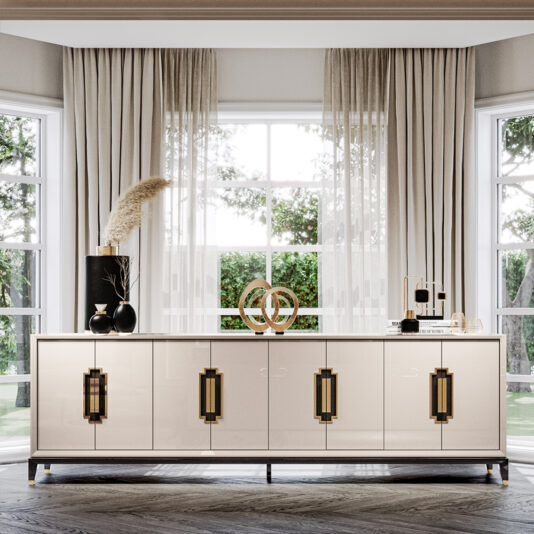 A modern, well-lit living room features a Large High End Lacquered Sideboard with gold-accented handles. The sideboard is adorned with decorative items, including a black vase with pampas grass, abstract sculptures, and an array of elegant jars. Large windows with sheer curtains frame the scene.