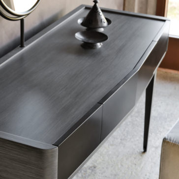 Modern Dressing Table With Mirror Introducing the Modern Dressing Table With Mirror, a contemporary gray-colored console table with sleek rounded corners and an elegant minimalist design. It features two drawers and a tabletop adorned with a stylish black tiered cone object. Perfectly positioned near a large window, this table allows natural light to beautifully illuminate your space.