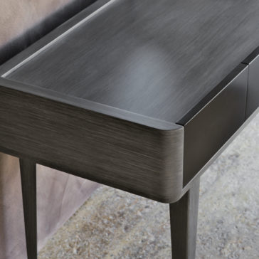 Modern Dressing Table With Mirror The Modern Dressing Table With Mirror boasts a sleek, contemporary design featuring curved edges and a matte finish. This wooden console stands gracefully on four slim legs and includes a drawer with a minimalist, handle-less design. The background features a textured wall and stone floor.