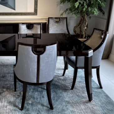 A dining area featuring a sleek, dark walnut table with a glossy surface and four Modern Walnut Luxury Dining Chairs, which have light gray upholstered backs and dark wooden frames. A large mirror and a tall green plant are visible in the background, creating an elegant ambiance.