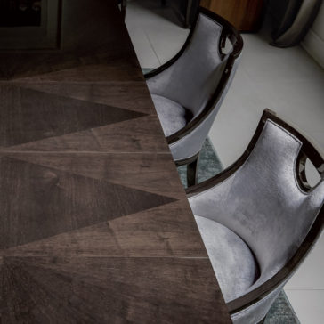 A sleek, modern dining table with a geometric wooden pattern is accompanied by two Modern Walnut Luxury Dining Chairs, featuring luxurious walnut seats and dark wooden frames. The light gray floor and part of a dark wooden cabinet are visible in the background, enhancing the contemporary interior design.