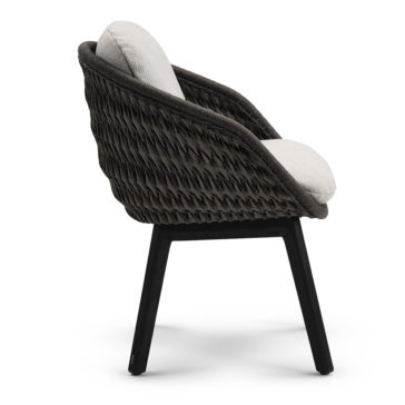 The Contemporary Outdoor Woven Dining Chair boasts a black woven frame paired with beige cushions on both the seat and backrest. It stands sturdily on four slightly angled legs and features a curved backrest that seamlessly transitions into armrests. This design expertly combines modern and rustic elements for a chic outdoor seating solution.