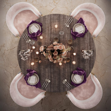 Round Modern Ribbed Veneer Dining Set The Round Modern Ribbed Veneer Dining Set comprises a round table with ribbed veneer and four pink velvet chairs, elegantly adorned with a centerpiece of pink roses and purple napkins. Each place setting features a white plate, menu, cutlery, and glassware. The wooden tabletop is thoughtfully decorated with candles and small ornaments surrounding the floral arrangement.