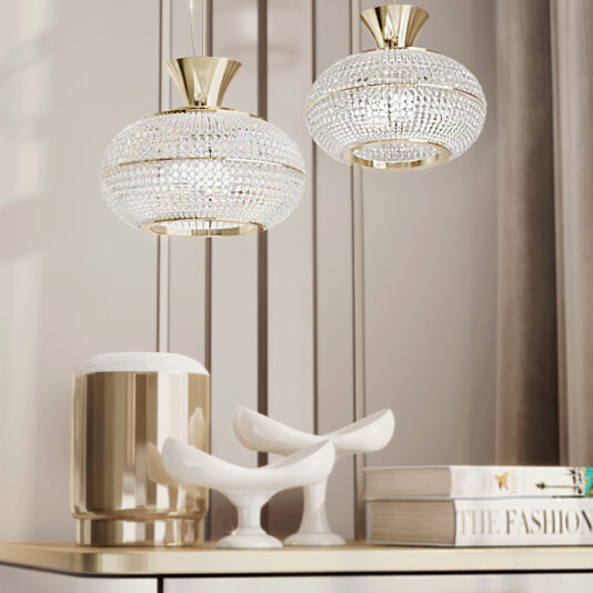 A modern interior with two Contemporary Crystal Pendant Lights suspended from the ceiling. Below, a minimalist white cabinet holds white ceramic bird sculptures, a stack of fashion books, and a gleaming gold vase. Light streams softly from the side.