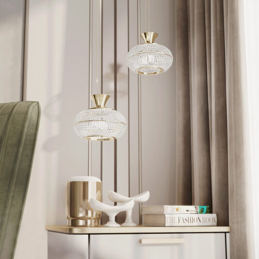Contemporary Crystal Pendant Light A stylish interior scene features two Contemporary Crystal Pendant Lights suspended from the ceiling. Below, a cabinet holds a gold-accented container, white decorative sculptures, and a stack of books. A green chair is partly visible next to a beige curtain.