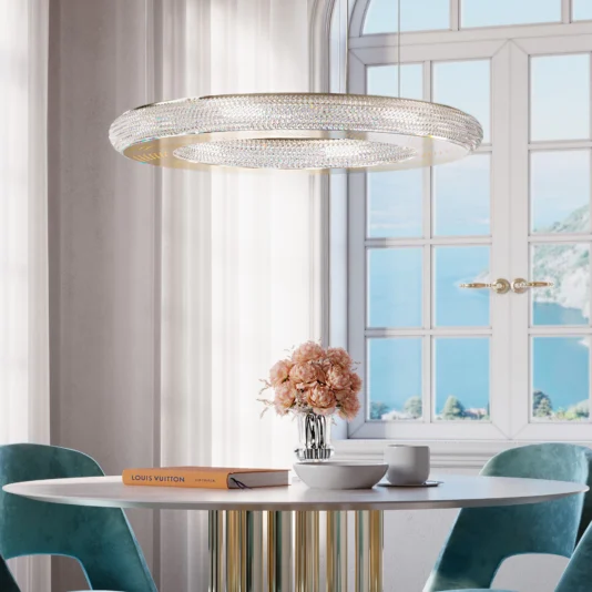 Modern Crystal Hoop Chandelier An elegant dining area features a round white table with pink flowers in a vase, a Louis Vuitton book, and teal chairs. The Modern Crystal Hoop Chandelier provides a soft glow from above, complemented by large windows that offer scenic views.