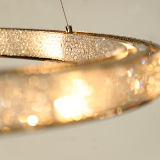 Modern Crystal Hoop Chandelier The image features a close-up of the Modern Crystal Hoop Chandelier, showcasing its shimmering crystals that softly glow with golden light. The focus is on the elegant rings, highlighting the intricate details and reflections of the crystals against a blurred background.