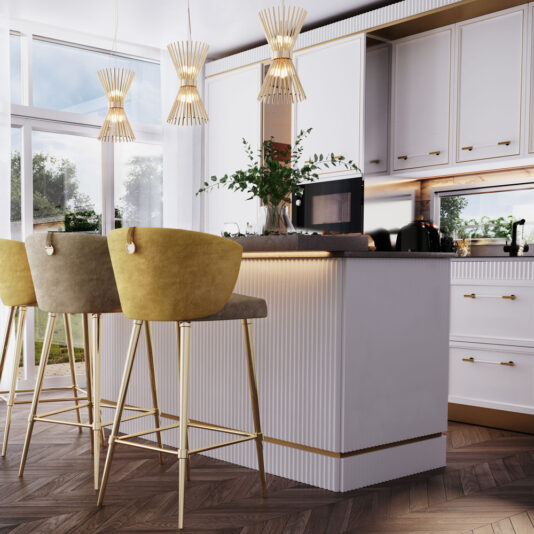 Modern Gold Plated Pendant Light A modern kitchen features a white island with gold accents and two green velvet barstools. Above the island, three Modern Gold Plated Pendant Lights add a touch of elegance. The kitchen boasts white cabinets, a microwave, and a coffee machine, with a window in the background letting in natural light.