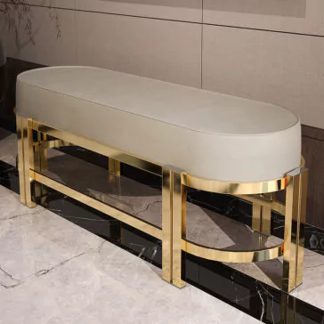 Modern Oval Leather Bench The Modern Oval Leather Bench, featuring a sleek gray upholstered seat and a modern gold metallic frame, sits against a tiled wall on a marble floor. With its polished finish, this stylish and contemporary bench exudes luxury.