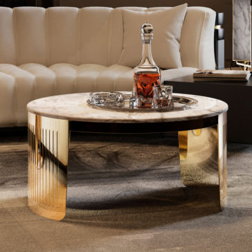 A luxurious living room scene showcases the exquisite Modern Marble Round Coffee Table with its elegant gold legs. Adorning the table is a crystal decanter filled with amber liquid, accompanied by two matching glasses neatly placed on a silver tray. In the background, a plush, cream-colored sofa adds to the opulent ambiance.