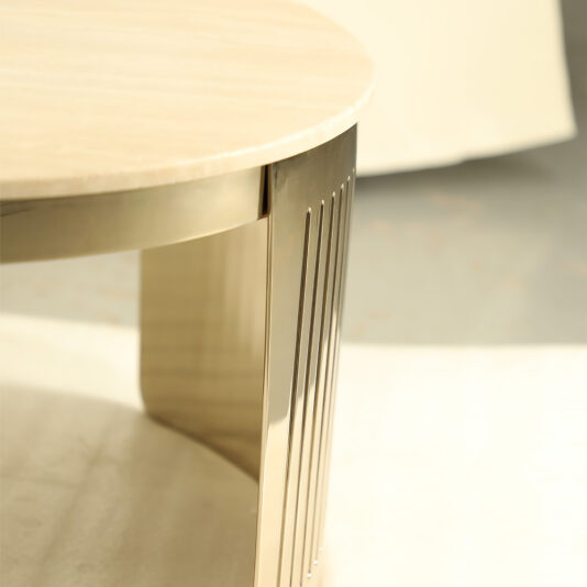 Modern Marble Round Coffee Table A close-up shot of a Modern Marble Round Coffee Table, showcasing its elegant marble top and sleek, metallic legs. The sunlight casts subtle shadows on the floor, adding depth to the image. The design of the legs features vertical indentations for a stylish touch.