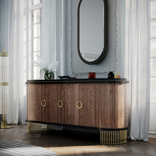 A stylish wooden sideboard with three circular brass handles and a black top stands against a wall. Above the Oval Veneer 3 Door Buffet hangs an oval mirror. To the left is a cylindrical floor lamp. White curtains frame large windows, and a vase with white feathers decorates the sideboard.