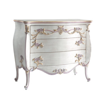 The Carved Italian Chest Of Drawers features an ornate, vintage-style design with a distressed white finish. It boasts a curved front and four drawers, each adorned with intricate floral carvings and gold accents. The dresser stands elegantly on four slender, curved legs.