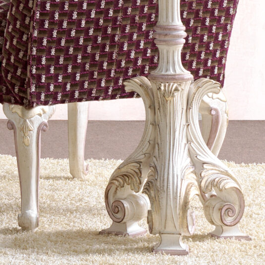 Carved Italian Floor Lamp A vintage-style table with an intricately carved white pedestal base on a textured beige rug. Surrounding the table are maroon cushioned chairs with a checkered pattern, all illuminated by the **Carved Italian Floor Lamp**. The floor is a warm brown color, and the background features a light pink wall.