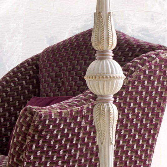 Carved Italian Floor Lamp A close-up of a maroon and beige woven pattern armchair with the Carved Italian Floor Lamp in white and gold in the foreground. The lamp features intricate detailing with leaf-like designs. The armchair is placed against a light-colored wall.