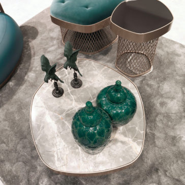 Contemporary Low Marble Coffee Table A contemporary low marble coffee table, adorned with two ornate green jars and two small bird sculptures, sits in the center. Around it are wireframe stools featuring cushioned seats, all positioned on a plush, light-colored rug.