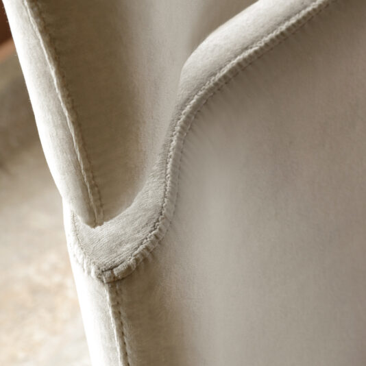 Close-up of a beige upholstered chair featuring detailed stitching along the edges. The image captures the smooth texture akin to that found on the Contemporary Upholstered Velvet Bed, with precise, neat seams that highlight the craftsmanship and quality of the upholstery.
