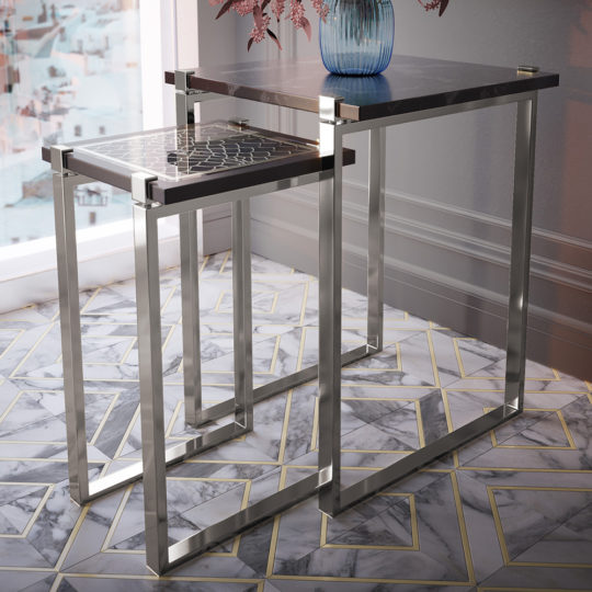 A contemporary decorative arrangement showcasing the Luxury Art Deco Inspired Nest of Tables, featuring metallic frames and sleek marble tops. The design allows the smaller table to slide under the larger one effortlessly. They are placed on a geometric-patterned marble floor, adjacent to a window and a wall accented with a blue vase filled with pink flowers.
