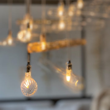 A close-up image showcases several hanging lights from the Modern Glass Lozenge Spiral Chandelier collection, featuring intricately designed glass bulbs that mimic spiral chandeliers. The softly glowing lights create a warm ambiance, while the blurred background accentuates the detailed patterns and textures of the glass bulbs.