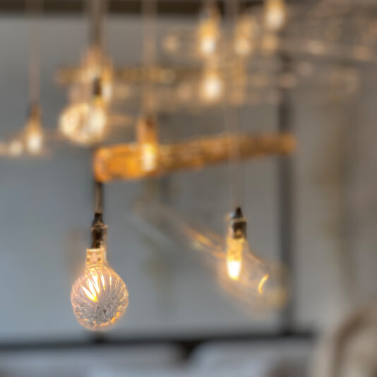 A close-up image showcases several hanging lights from the Modern Glass Lozenge Spiral Chandelier collection, featuring intricately designed glass bulbs that mimic spiral chandeliers. The softly glowing lights create a warm ambiance, while the blurred background accentuates the detailed patterns and textures of the glass bulbs.