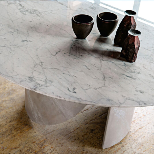 The Modern Italian Marble Dining Set showcases a round table with striking gray veining, complemented by three dark ceramic cups and an assortment of two wooden vases in different sizes. Its distinctive base rests gracefully on a floor featuring a subtle, textured design.