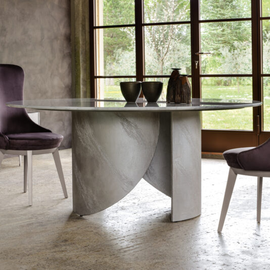 A contemporary dining room showcasing a glass-top table with an eye-catching, sculptural gray base. The table, included in the Modern Italian Marble Dining Set, is surrounded by stylish purple upholstered chairs. Expansive windows in the background provide a refreshing view of the greenery outside, amplifying the room's tranquil ambiance.