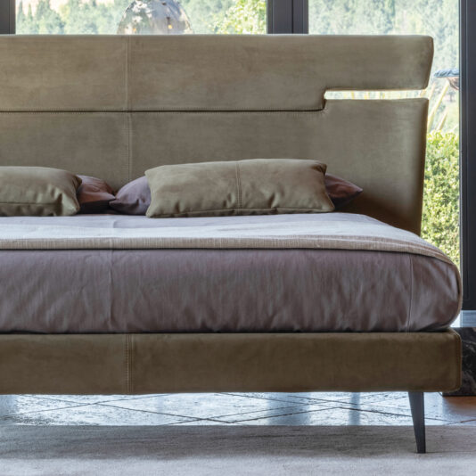 Modern Upholstered Velvet Bed A contemporary bedroom arrangement showcasing a Modern Upholstered Velvet Bed with a tall, sleek headboard positioned against expansive windows. The bed is adorned with matching tan pillows, and the softly lit natural outdoor backdrop is visible through the windows.