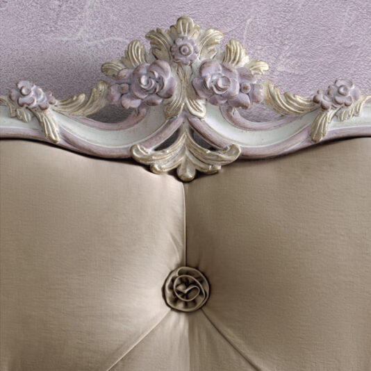Rococo Style Button Upholstered Bed The Rococo Style Button Upholstered Bed features an ornate headboard adorned with a beige cushion and a floral design in pastel colors set against a light lavender textured wall. The detailed carving at the top includes roses and intricate scrollwork, while a fabric flower accent in the center of the cushion enhances its elegance.