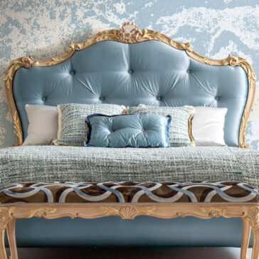 Button Upholstered Rococo Style Bed A luxurious bedroom features a large Rococo-style headboard with button upholstery. The bed is adorned with textured blue and white pillows, complemented by a patterned blanket, set against a blue and white textured wall. Product: Button Upholstered Rococo Style Bed.
