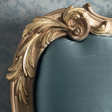 Button Upholstered Rococo Style Bed Close-up of an ornate, gold-painted wooden frame with intricate scrollwork and leaf patterns, surrounding a smooth, teal-colored fabric surface that evokes the style of a Button Upholstered Rococo Style Bed. The background features a textured grayish-blue wall.