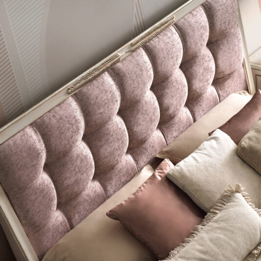 A close-up of the Feather Design Button Upholstered Sleigh Bed showcases its plush, tufted pink headboard adorned with braided rope trim at the top, featuring feather design buttons. The bed is elegantly made up with light cream and pink pillows, some fringed, all arranged neatly to create a sophisticated and cozy atmosphere.